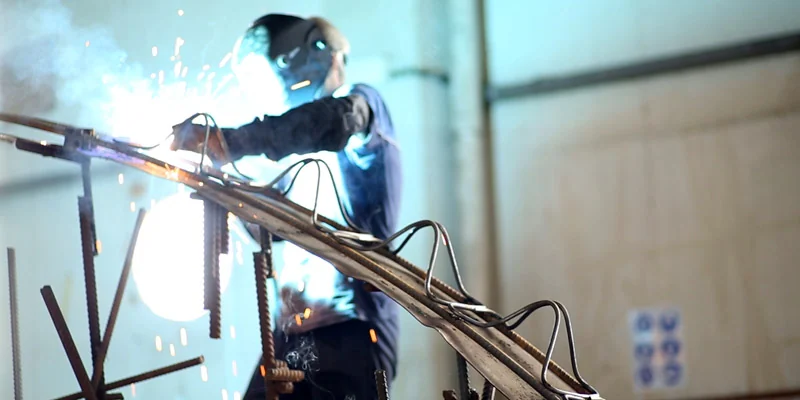 Manufacturer photograph of a curved lattice girder being welded in a workshop