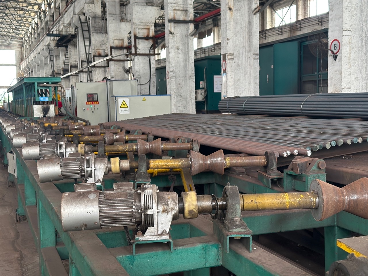 Driven hourglass rollers beside round bars on the JOTAIN heat-treatment line