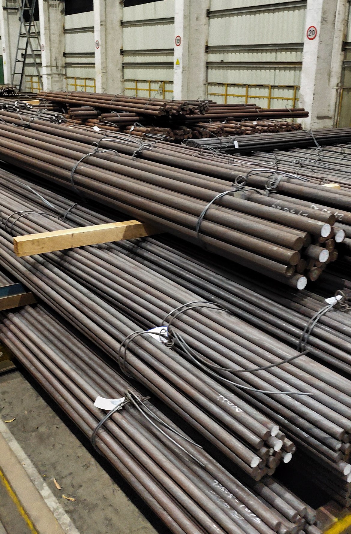 Multiple bundles of long round steel bars inside a warehouse